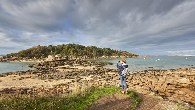 Un femme se tient debout et prend des photos de l'Ile Milliau depuis la Pointe du Castel à Trébeurden