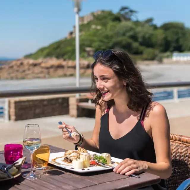 Smiling woman sitting on a terrace, holding a wine glass and looking at the horizon