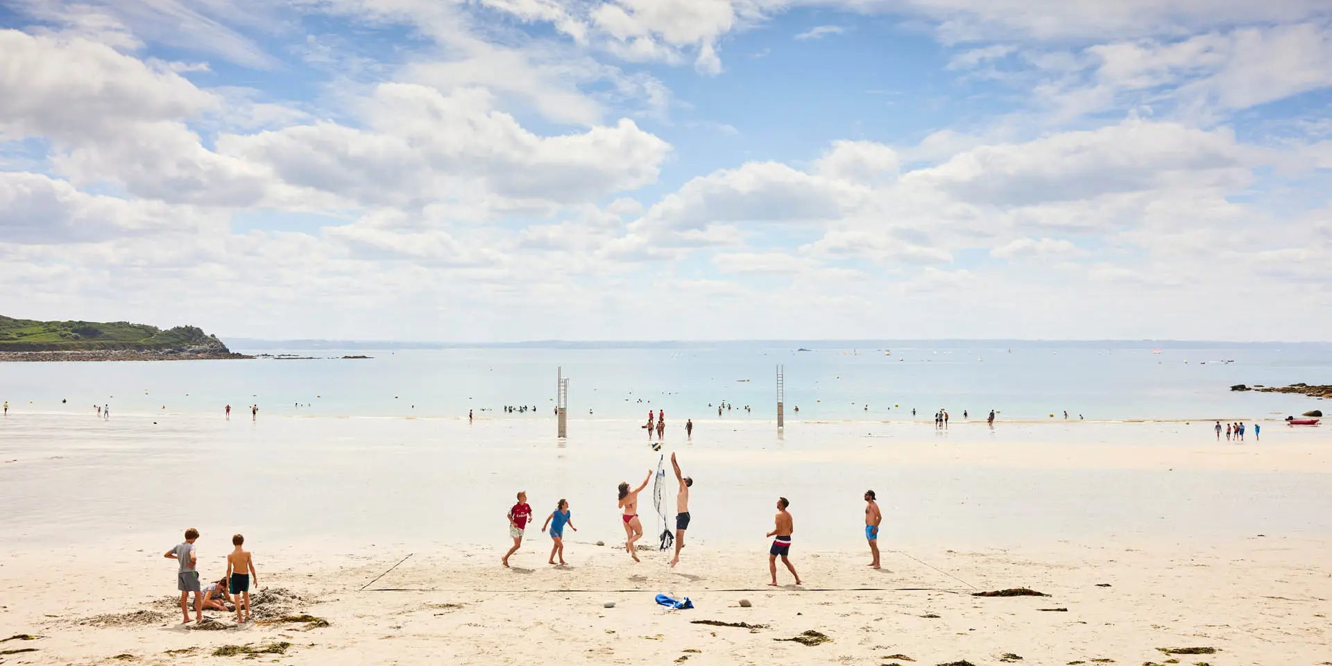 Beach with people walking, playing, and relaxing under a partly cloudy blue sky