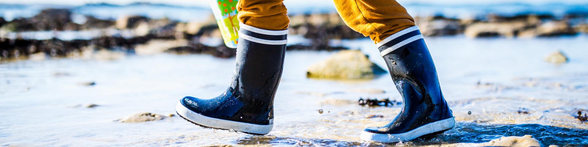 Un enfant marche sur la plage. Il porte des bottes de marin bleues et un cirée jaune