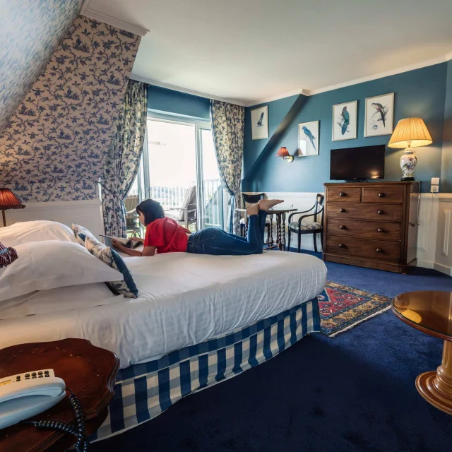 Une femme lit un magazine sur le lit d'une chambre cosy avec terrasse de l'Hôtel Spa - Ti al Lannec, à Trébeurden