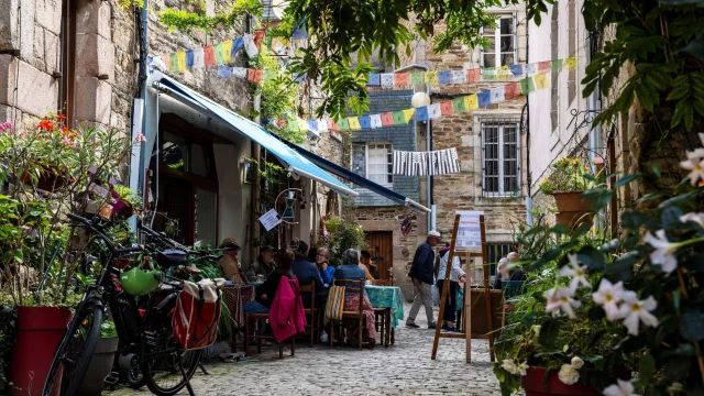Des personnes déjeunent en terrasse dans une venelle fleurie de Lannion