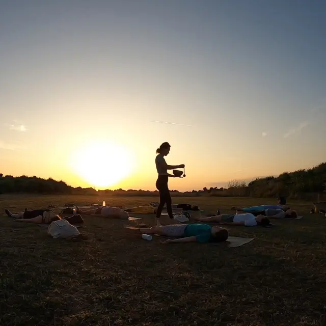 un groupe de personne pratique une séance de Yoga en plein-air au coucher du soleil