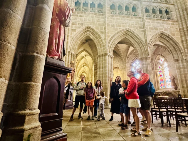 Balade ludique : les aventures d'Aldéric à Tréguier. Le groupe observe les détails architecturaux de l'intérieur de la cathédrale Saint Tugdual sous les commentaires de la guide