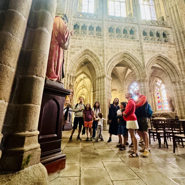 Balade ludique : les aventures d'Aldéric à Tréguier. Le groupe observe les détails architecturaux de l'intérieur de la cathédrale Saint Tugdual sous les commentaires de la guide