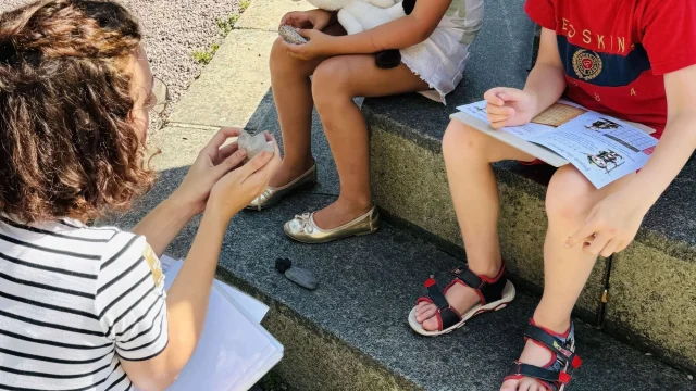 Balade Ludique de Lannion, la guide montre différentes pierres aux enfants afin qu'ils trouvent celle qui a permis de construire l'église Saint-Jan du Baly
