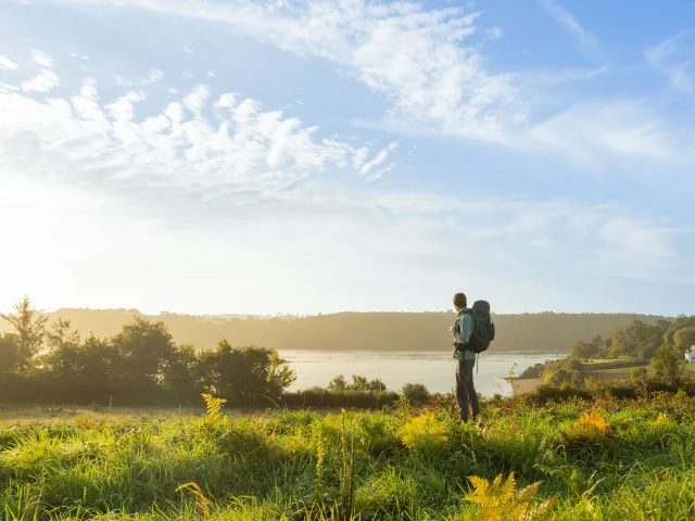 Un randonneur avec un sac à dos sur le GR34 regarde vers la mer.