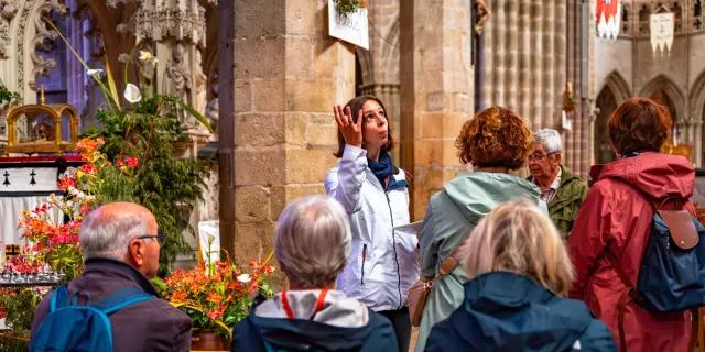 Une guide montre la nef d'une église à un groupe de touriste en visite guidée.