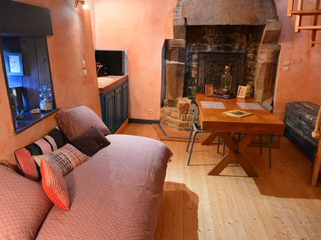 Intérieur d’un salon avec canapé beige, table basse en bois, cheminée en pierre avec une petite fen^tre au dessus du canapé