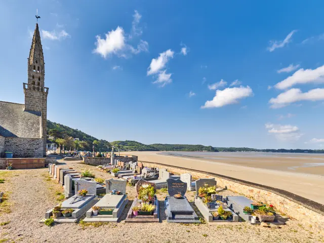 Un cimetière marin avec des tombes ornées de fleurs situées à côté d'une église, le tout face à la mer
