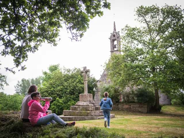 Deux personnes assises sur l'herbe dans un parc, avec une chapelle en arrière-plan et une petite fille qui court vers la chapele