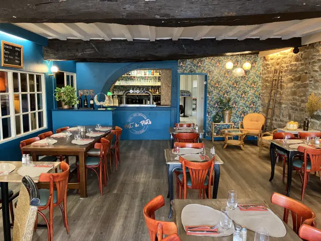 Intérieur d'un bar-restaurant avec des tables en bois et des chaises rouges, décoré de guirlandes lumineuses et de plantes