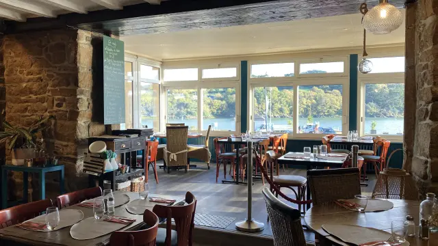 Terrasse de restaurant en bord de mer avec tables, chaises et voiliers amarrés