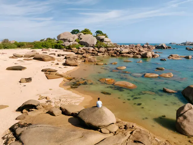White sandy beach lined with rounded rocks, with turquoise reflections on the shallow water