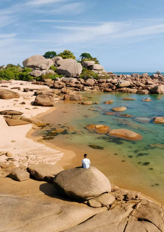 Weißer Sandstrand mit abgerundeten Felsen, türkisfarbene Reflexionen im flachen Wasser