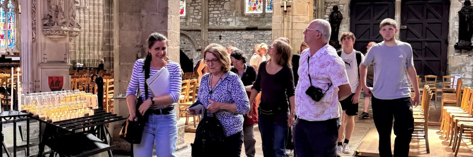 Groupe de touristes marchant à l'intérieur de la Cathédrale gothique de Tréguier avec des arches et des vitraux.
