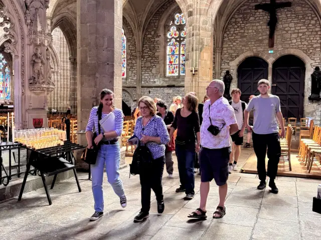 Groupe de touristes marchant à l'intérieur de la Cathédrale gothique de Tréguier avec des arches et des vitraux.